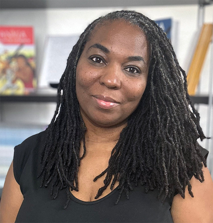 Children’s book author Jacquitta A. McManus, founder of Worlds To Discover, smiling in front of a bookshelf.